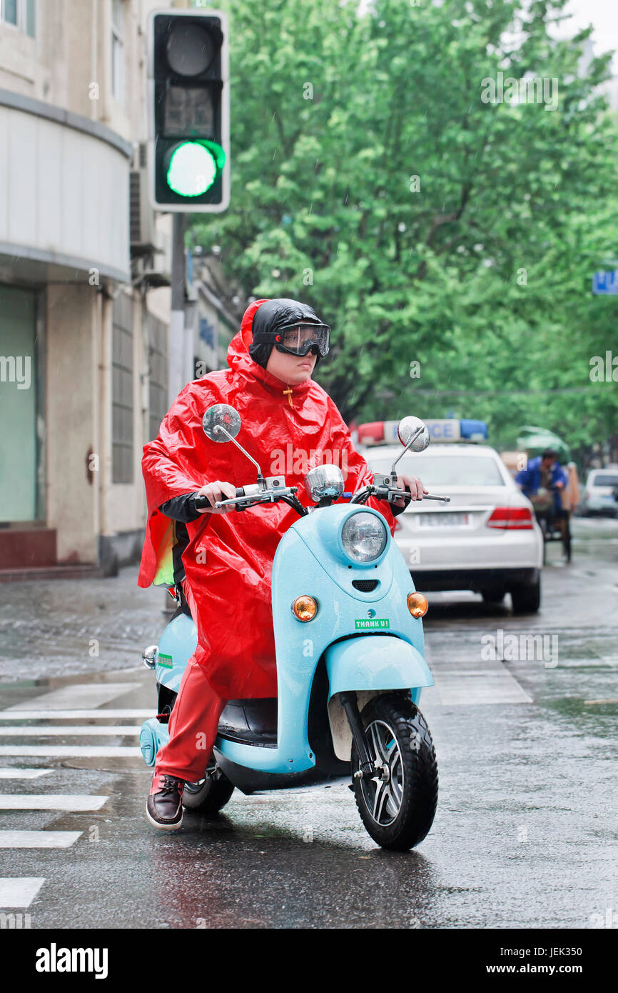 Chinese man in red rainwear on a retro scooter. Shanghai has a humid subtropical climate, its summer is very warm and humid. Stock Photo