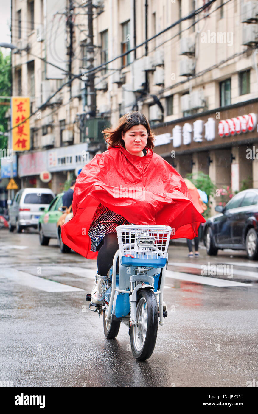 Chinese girl in red rainwear on an e-bike. Shanghai has a humid subtropical climate, its summer is very warm and humid. Stock Photo