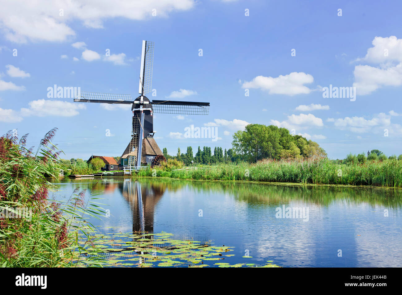 Ancient wooden windmill mirrored in a canal on a summer day with a blue sky and dramatic clouds. Stock Photo