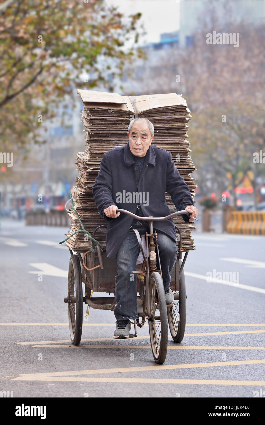YIWU-CHINA-JAN. 8, 2016. Senior man transports cardboard on a tricycle. Elderly population of China (60 or older) is currently about 128 million. Stock Photo