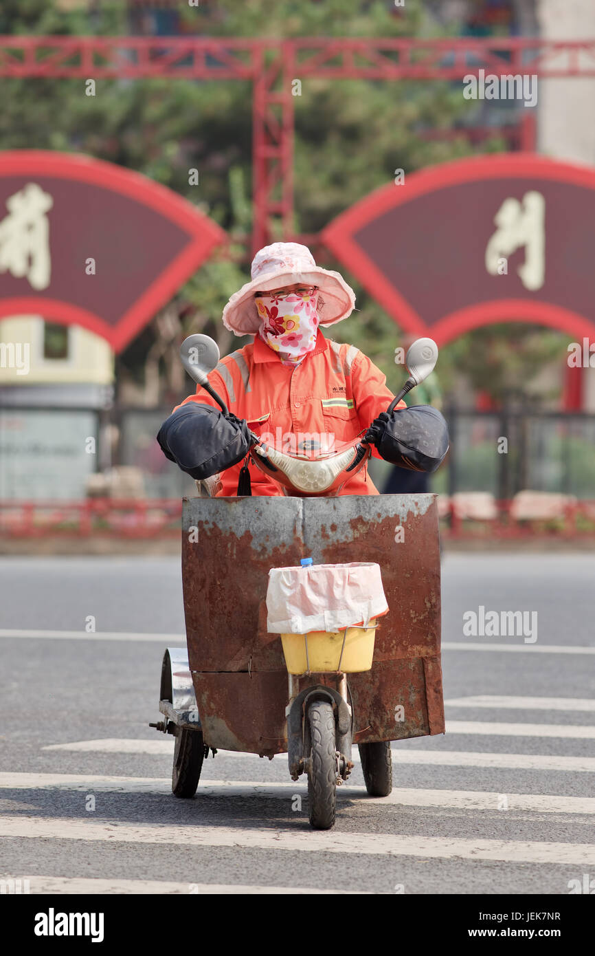 BEIJING-JUNE 9, 2015. Female street sweeper with mouth cap on electric trike. Thanks to an army of street sweepers Beijing city center is very clean. Stock Photo