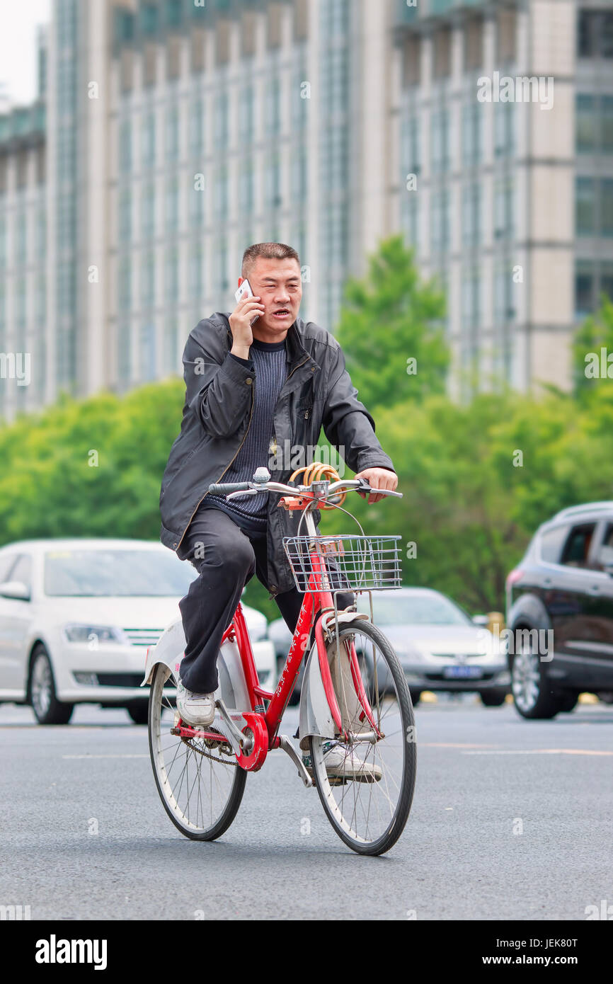 BEIJING-MAY 4, 2016. Chinese male senior make a phone call on the bike with traffic on the background. Stock Photo