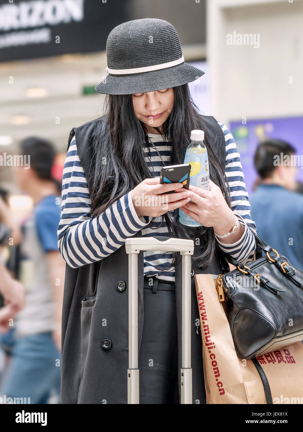 BEIJING-MAY 21, 2016. Fashionable dressed Chinese young girl busy with her smartphone inside a shopping mall. Stock Photo