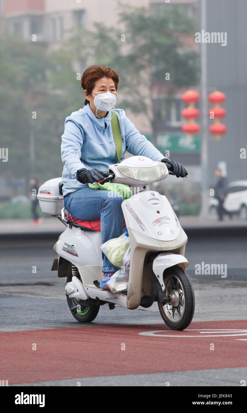 BEIJING-OCT. 11 ,2014. Woman on an e-bike in smog blanketed city. A concentration of PM2.5, small particles that poses a huge health risk. Stock Photo