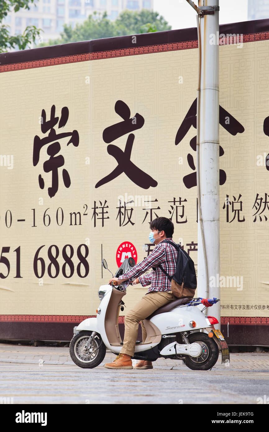 NANJING-MAY 25, 2014. Man on e-bike in front of wall with advertising. Outdoor advertising became China’s third largest medium after TV and print. Stock Photo
