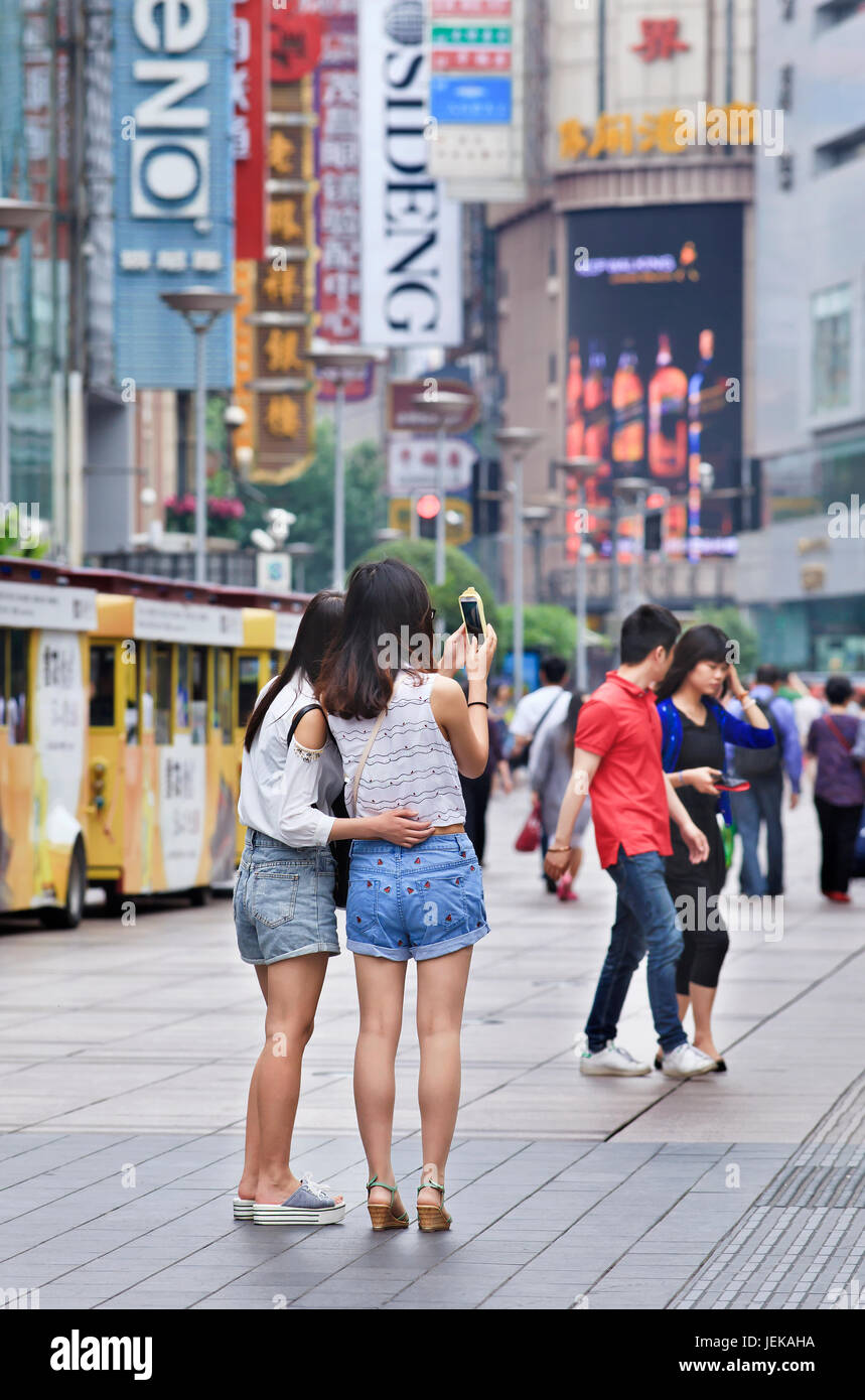 Girls in Nanjing East Shopping Street take a photo with their smart phone. It is the main shopping street of Shanghai. Stock Photo
