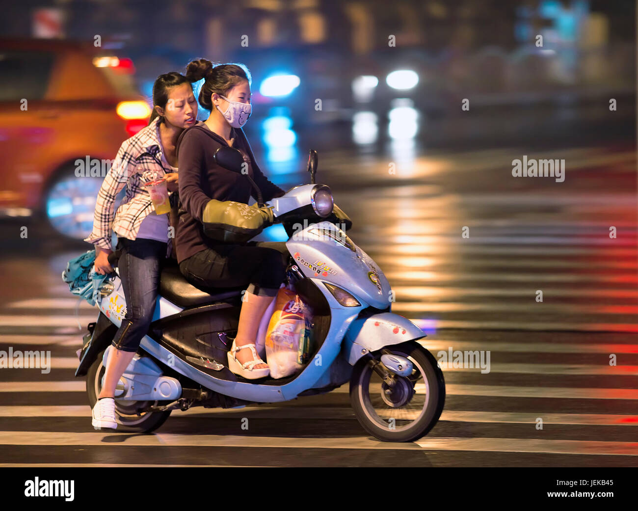 Chinese girls on electric bike at night. Electric bikes are swarming on the streets in China. Nationwide, there are about two hundred million. Stock Photo