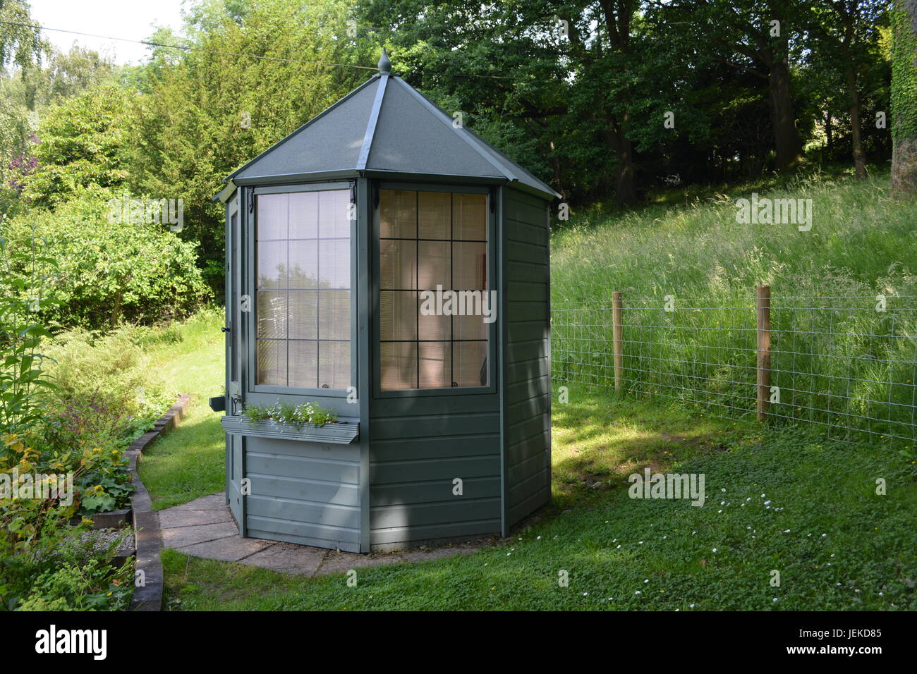 Octagonal painted wooden timber summer house summerhouse in lawned garden setting  with mesh wire stock cattle fence and woodland in background UK Stock Photo