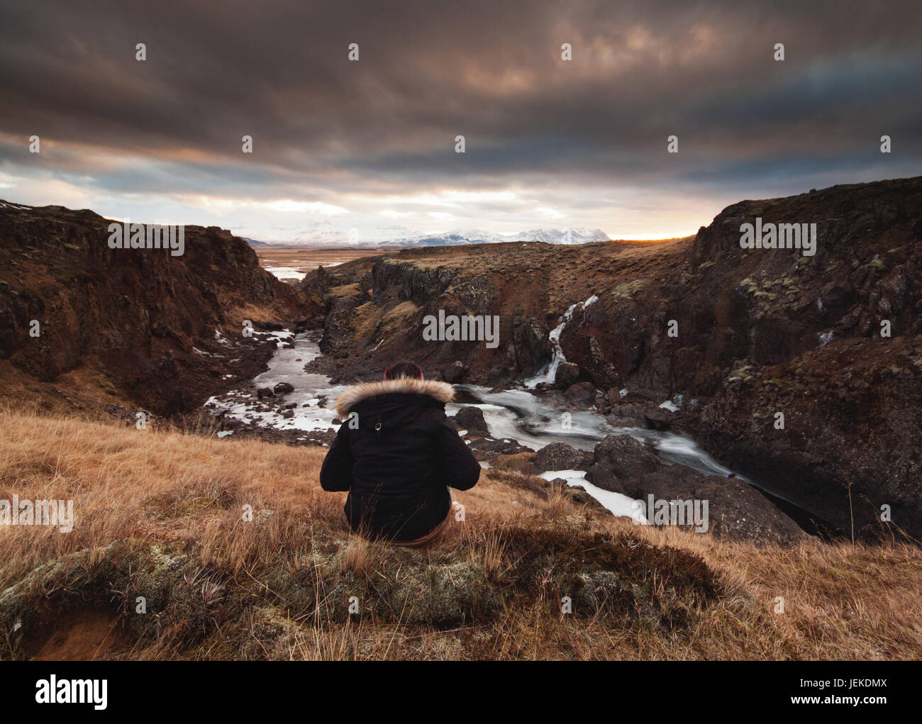 Woman sitting on rocks looking at sunset, Iceland Stock Photo