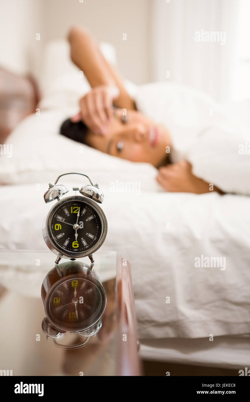 Alarm clock against brunette on bed Stock Photo