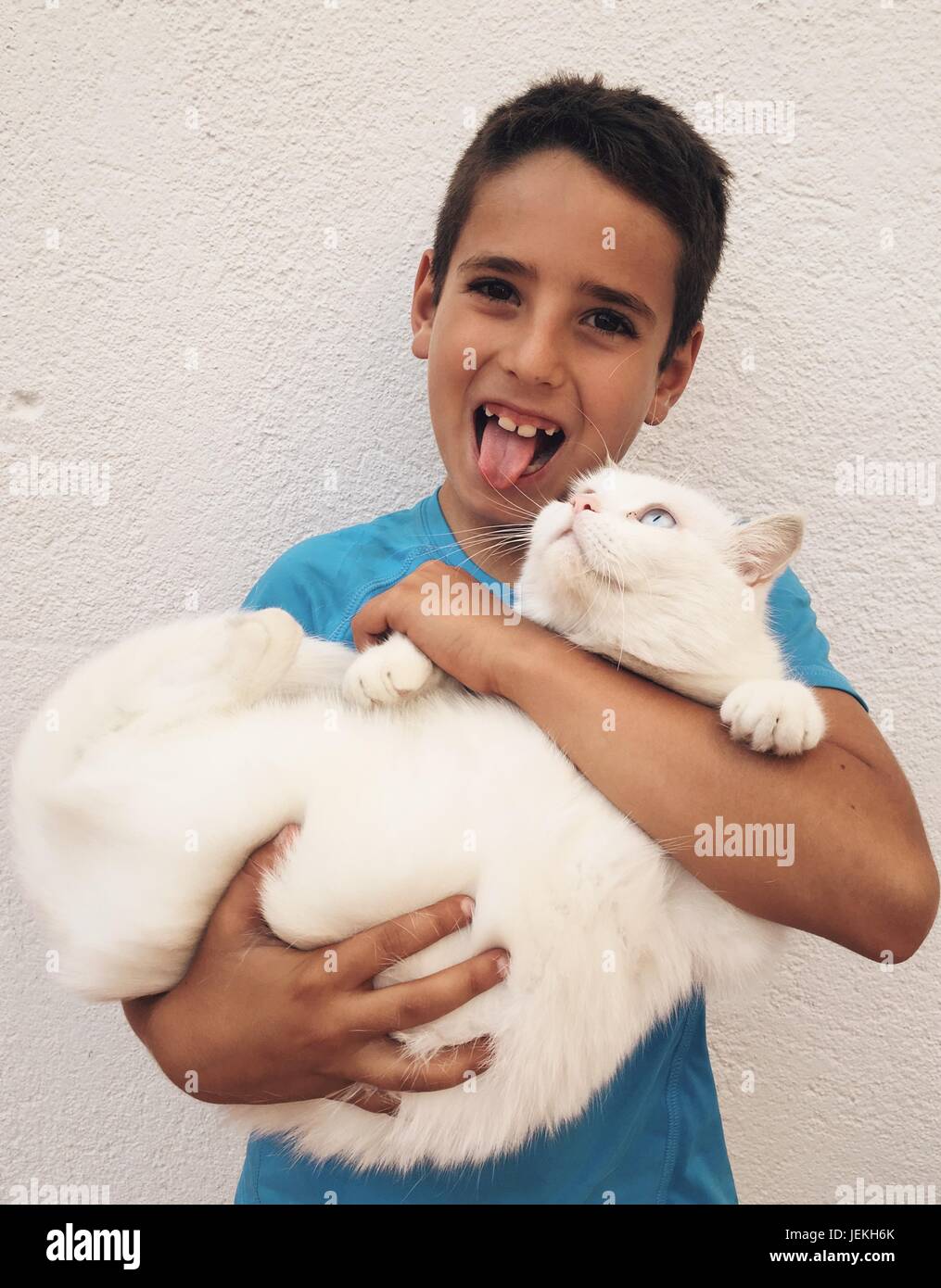 Boy pulling funny faces cuddling a cat Stock Photo