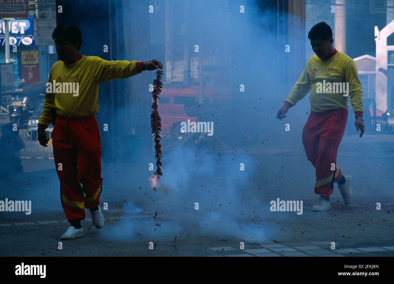 Thailand, North, Chiang Mai, Chinese New Year. Man holding chain of fire crackers ignited at one end partly obscured by smoke. Stock Photo