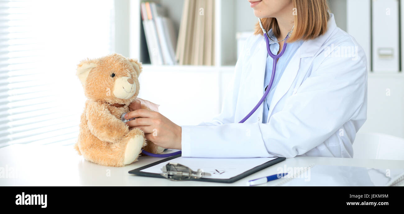 Female doctor examining a Teddy bear patient by stethoscope. Children ...