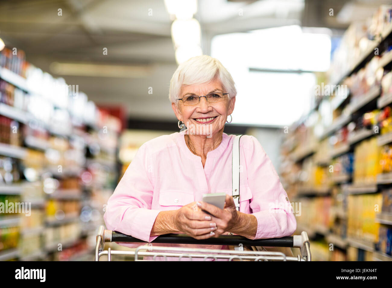 Senior woman using phone while pushing cart Stock Photo - Alamy