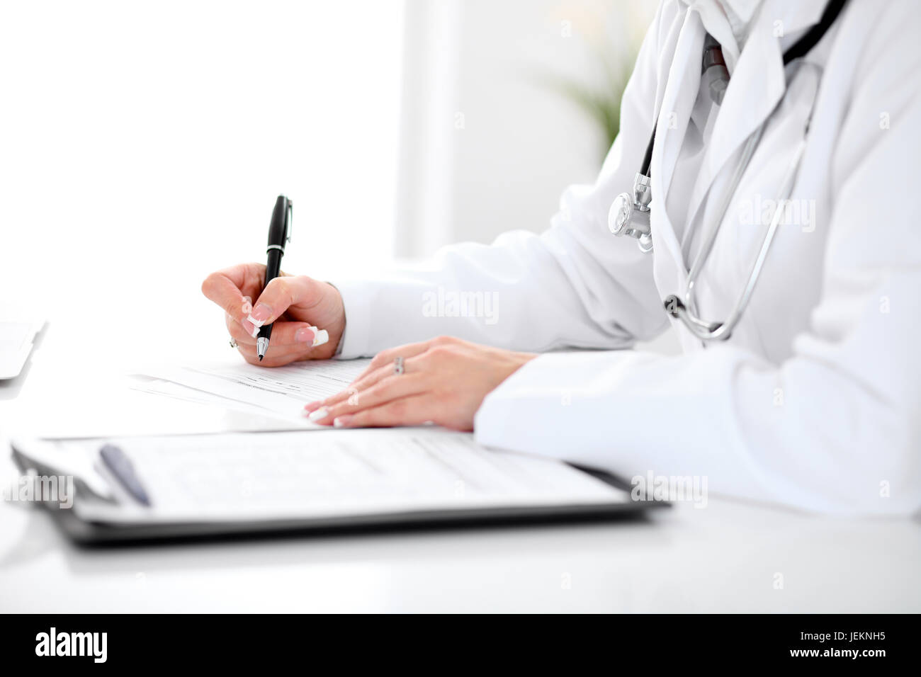 Close-up of a female doctor filling out application form , sitting at ...