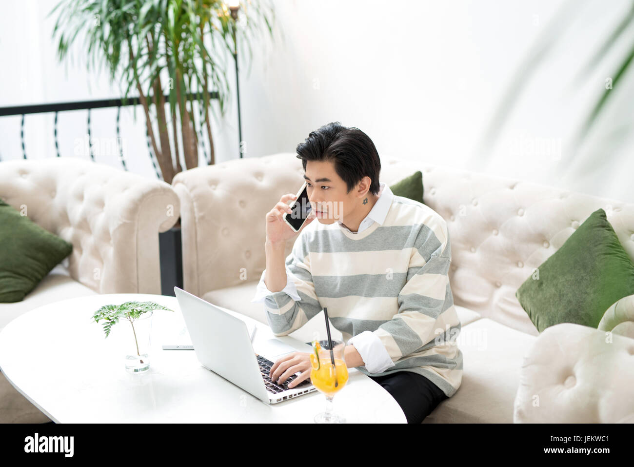 Asian businessman using mobile phone while working with laptop on table ...