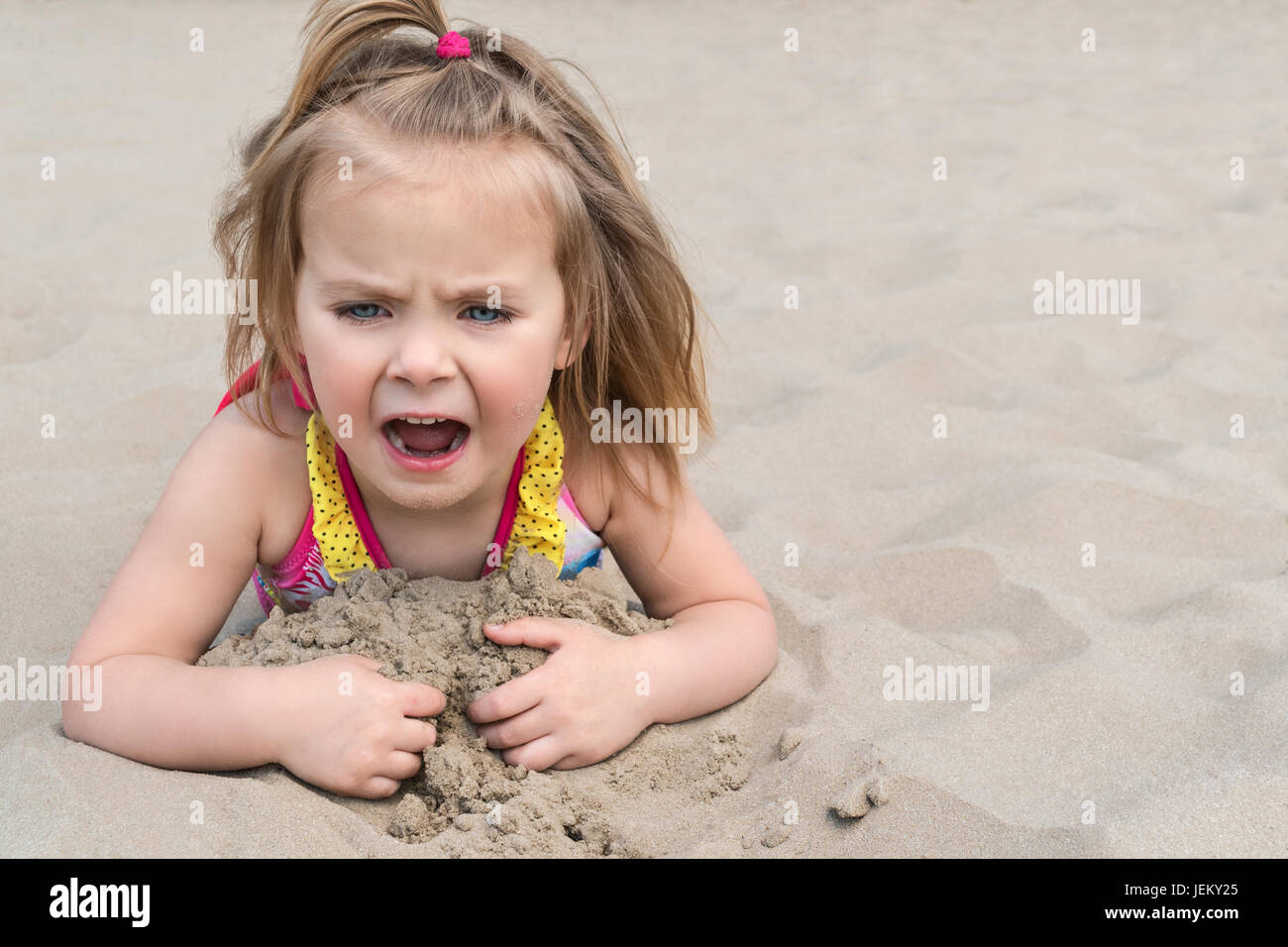 Little girl lying on the sand on the beach screaming mouth wide open