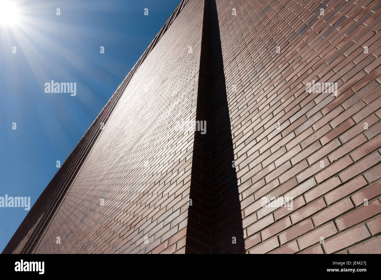 Red brick wall facade against blue sky and sun beams. Stock Photo