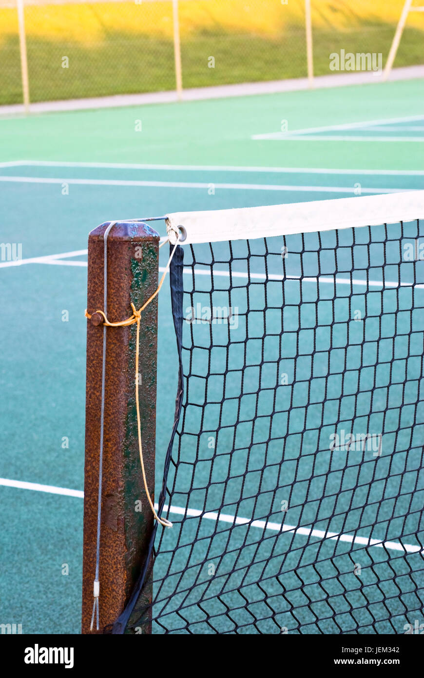 Tennis court net attached to rusting metal post with yellow and grey