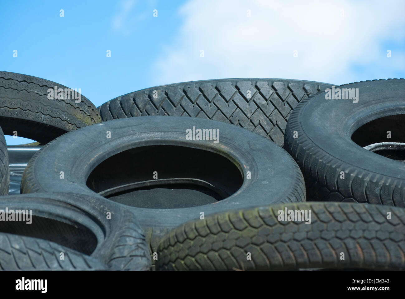 A recycle pile of used rubber car tyres, with blue sky and fluffy white clouds in the background. Stock Photo