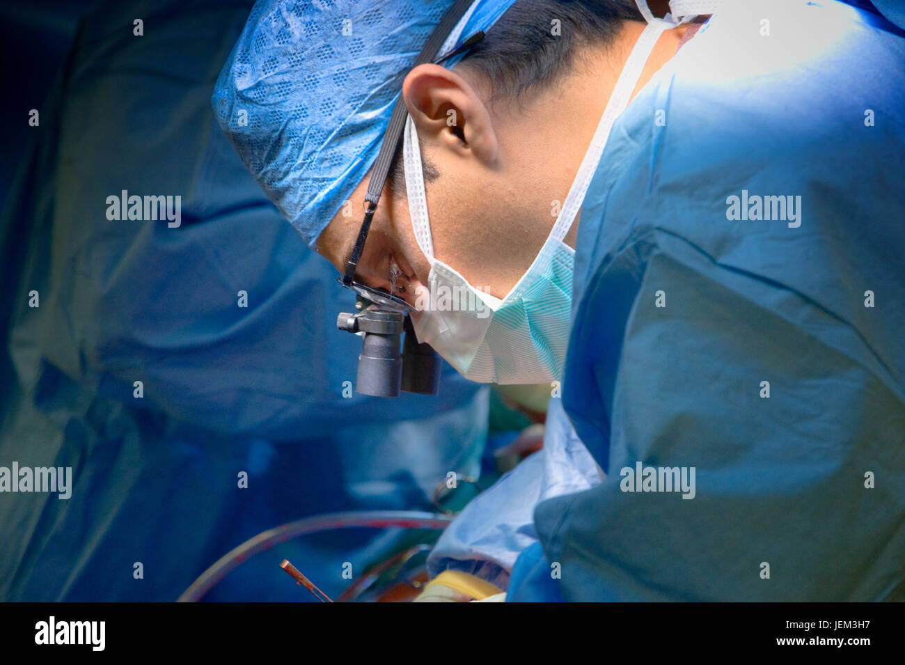 A surgeon operating on a patient wears surgical binocular loupes which magnify the working area and increase precision. Stock Photo