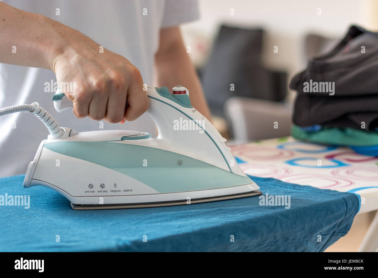 An iron on an ironing board with a blue shirt close up from the side
