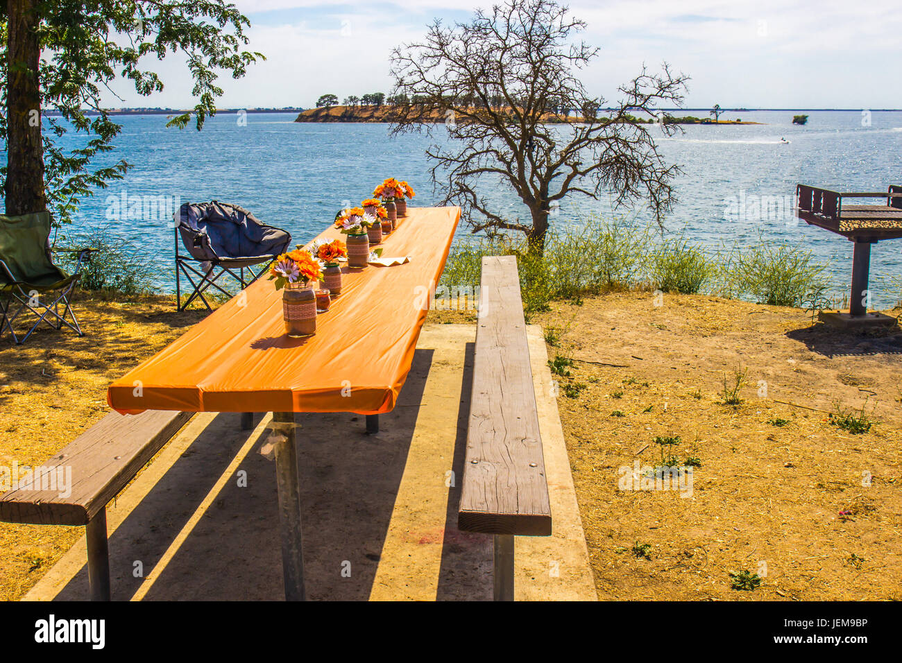 Decorated Picnic Table & BBQ Stand On Lake With Island In Background