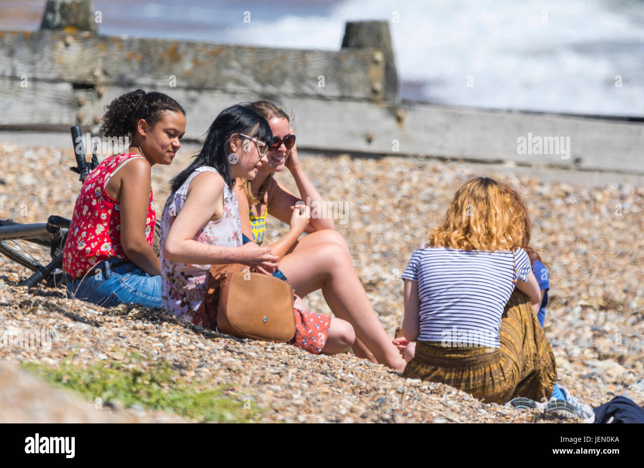 A group of young people of different ethnicities sitting on a beach together enjoying hot wearing at the seaside in Summer in the UK. Stock Photo