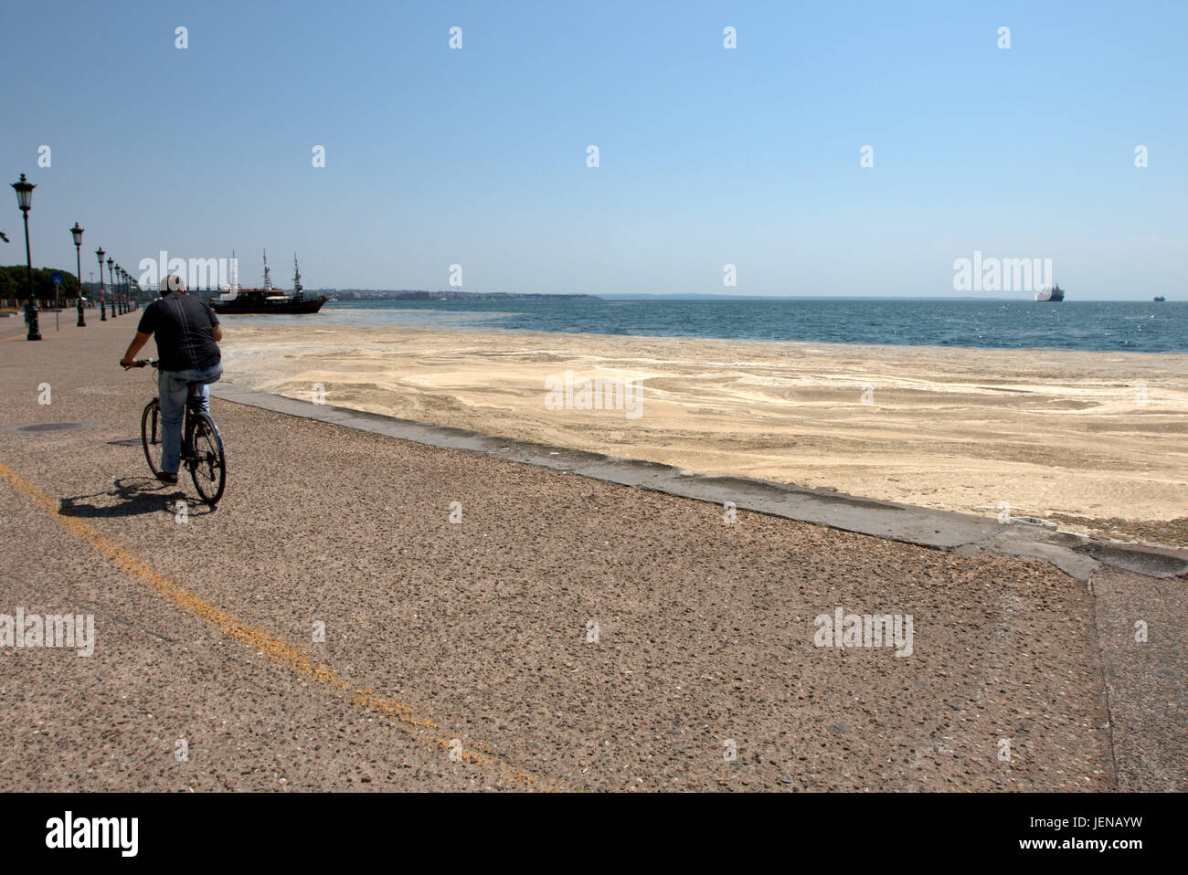 Thessaloniki, Greece. 27th June, 2017. A cyclist drives past the red tide affected seafront of the northern Greek port city of Thessaloniki. Red tide is a common name for a phenomenon known as an algal bloom, caused by species of dinoflagellates, taking on a red or brown colour. Credit Credit: Orhan Tsolak/Alamy Live News Stock Photo
