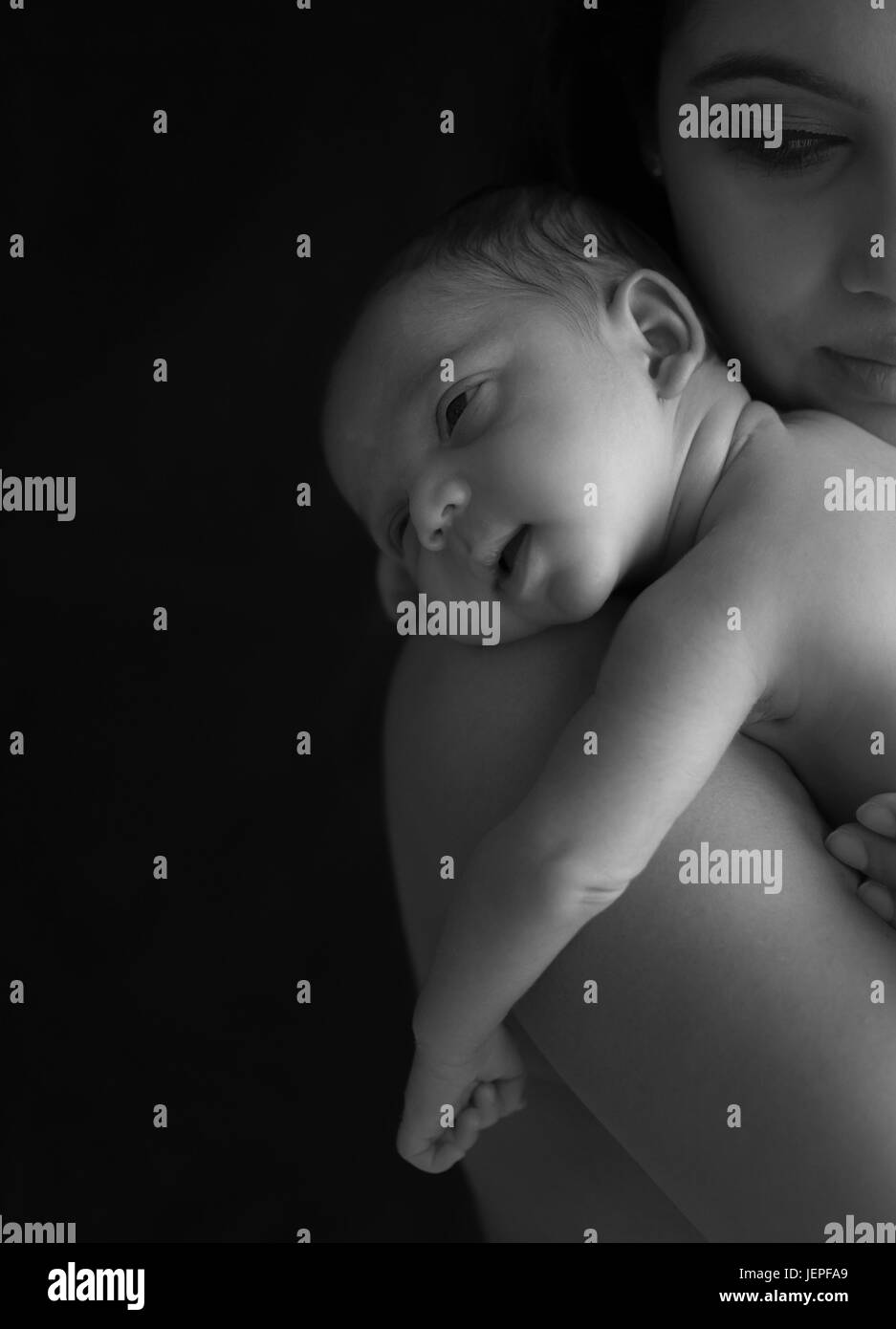 Model released photograph of a newborn baby boy smiling while resting his head on his mothers shoulders Stock Photo