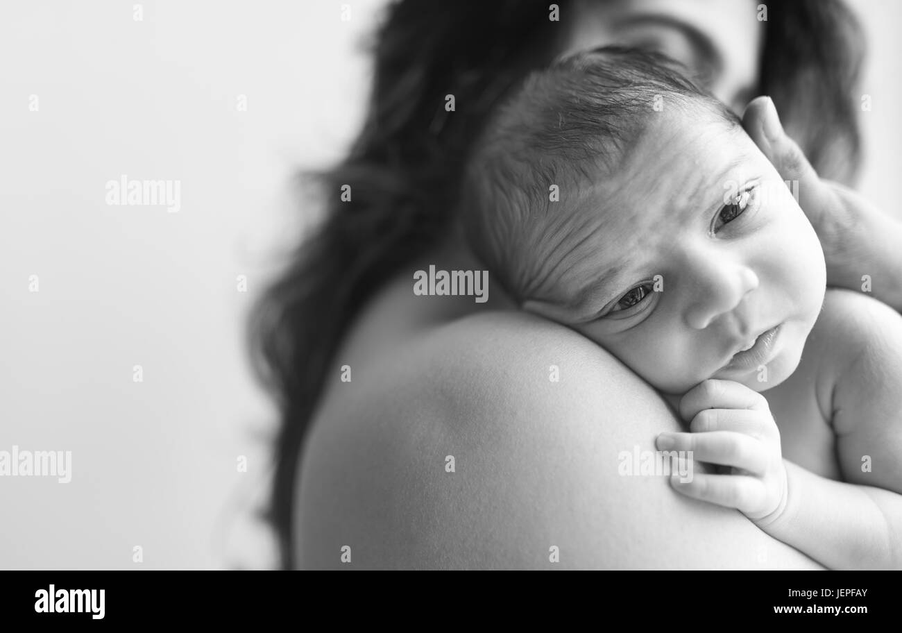 Model released photograph of a newborn baby boy with expressive eyes is resting on his mothers shoulders Stock Photo