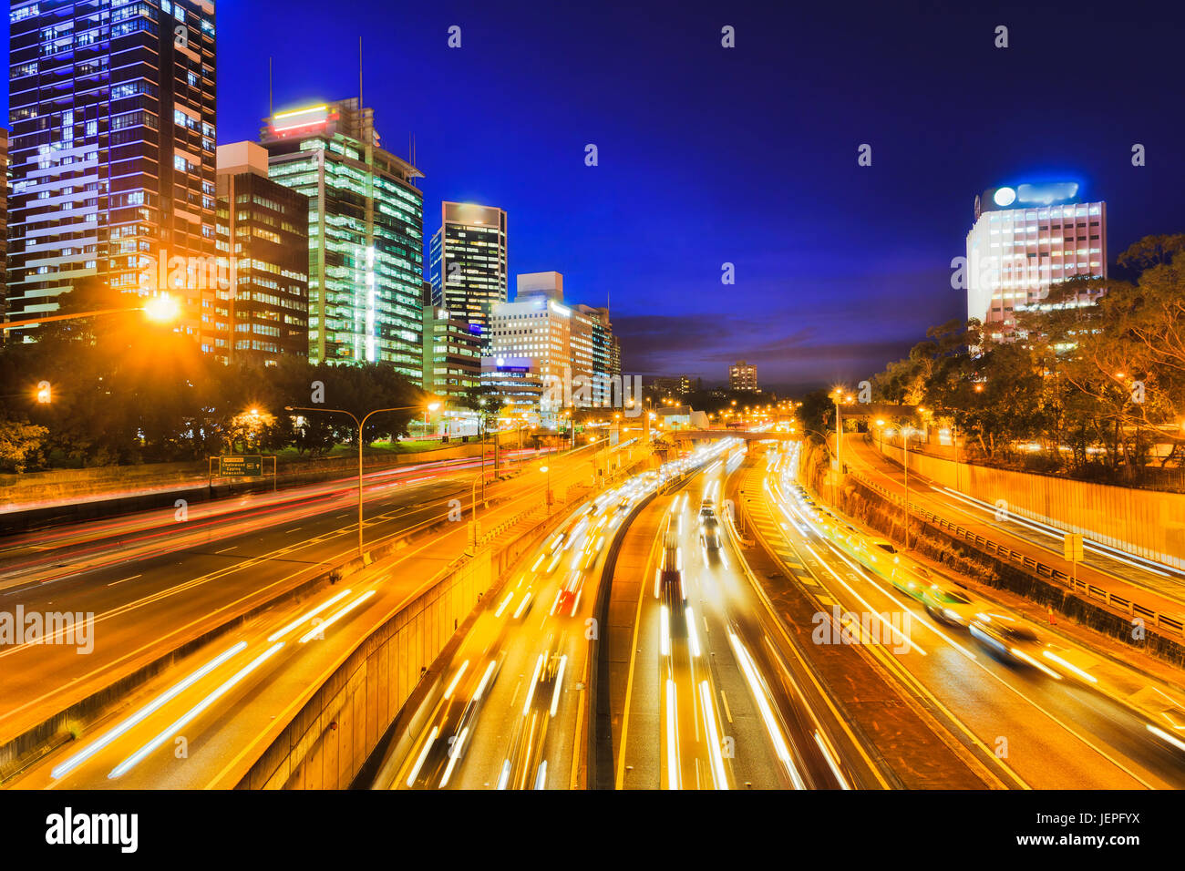 Wide multi-lane warringah freeway at the entrance to Sydney Harbour tunnel at late night with lots of commuting motor traffic between high-rise tower  Stock Photo