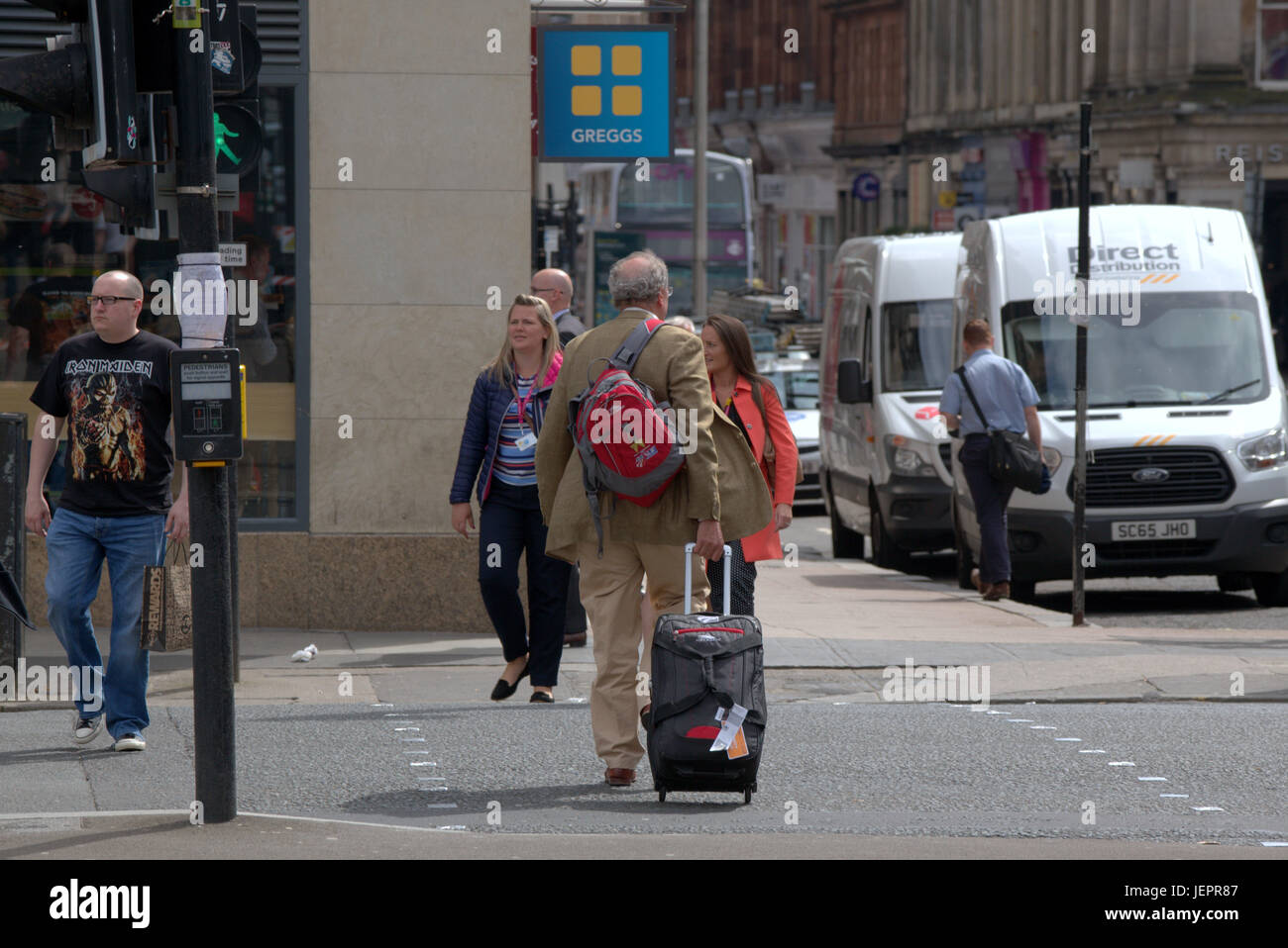 business man tourist with luggage trolley wheeled suitcase on the streets of Glasgow crossing road to destination or hotel Stock Photo