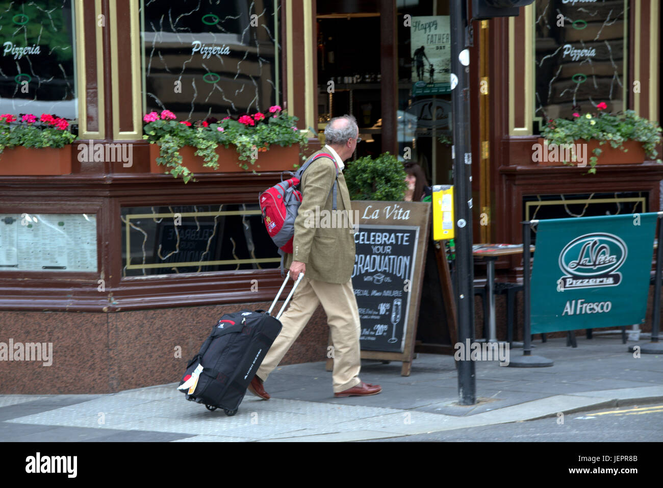business man tourist with luggage trolley wheeled suitcase on the streets of Glasgow crossing road to destination or hotel Stock Photo