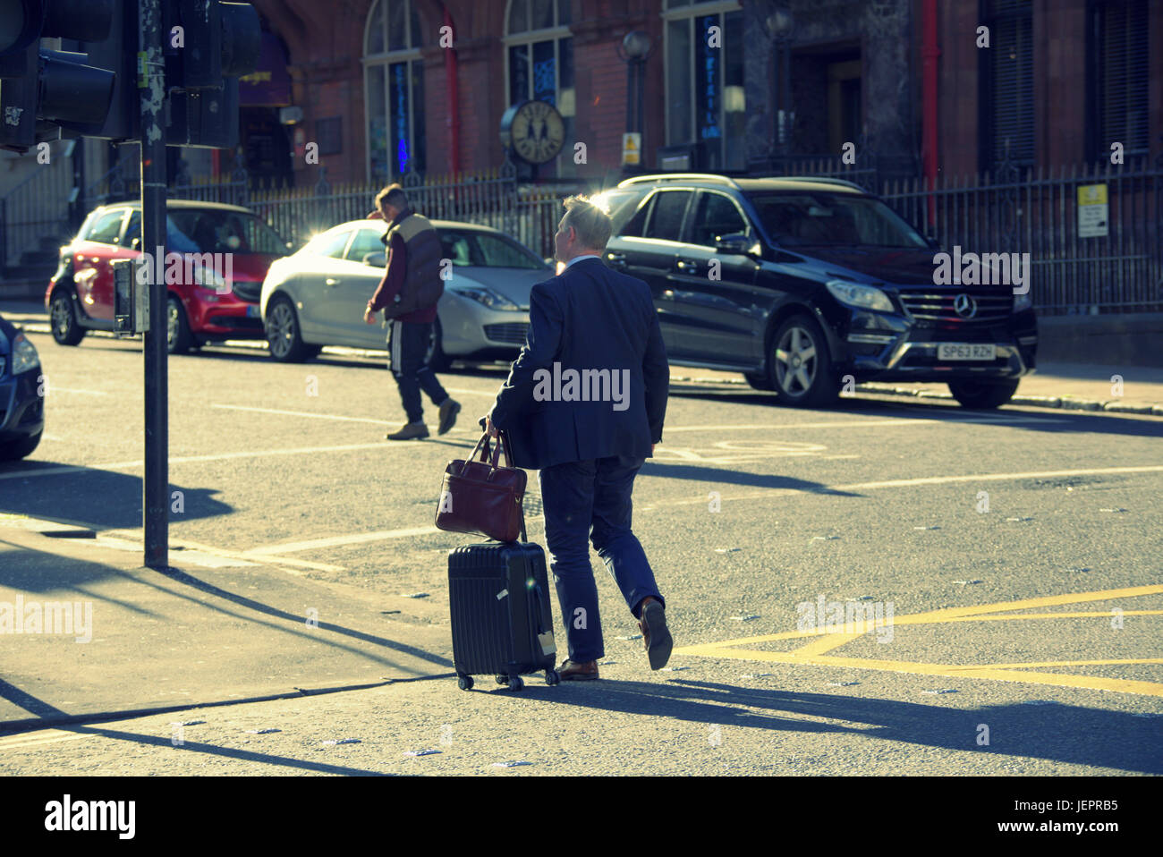 business man tourist with luggage trolley wheeled suitcase on the streets of Glasgow crossing road to destination or hotel Stock Photo