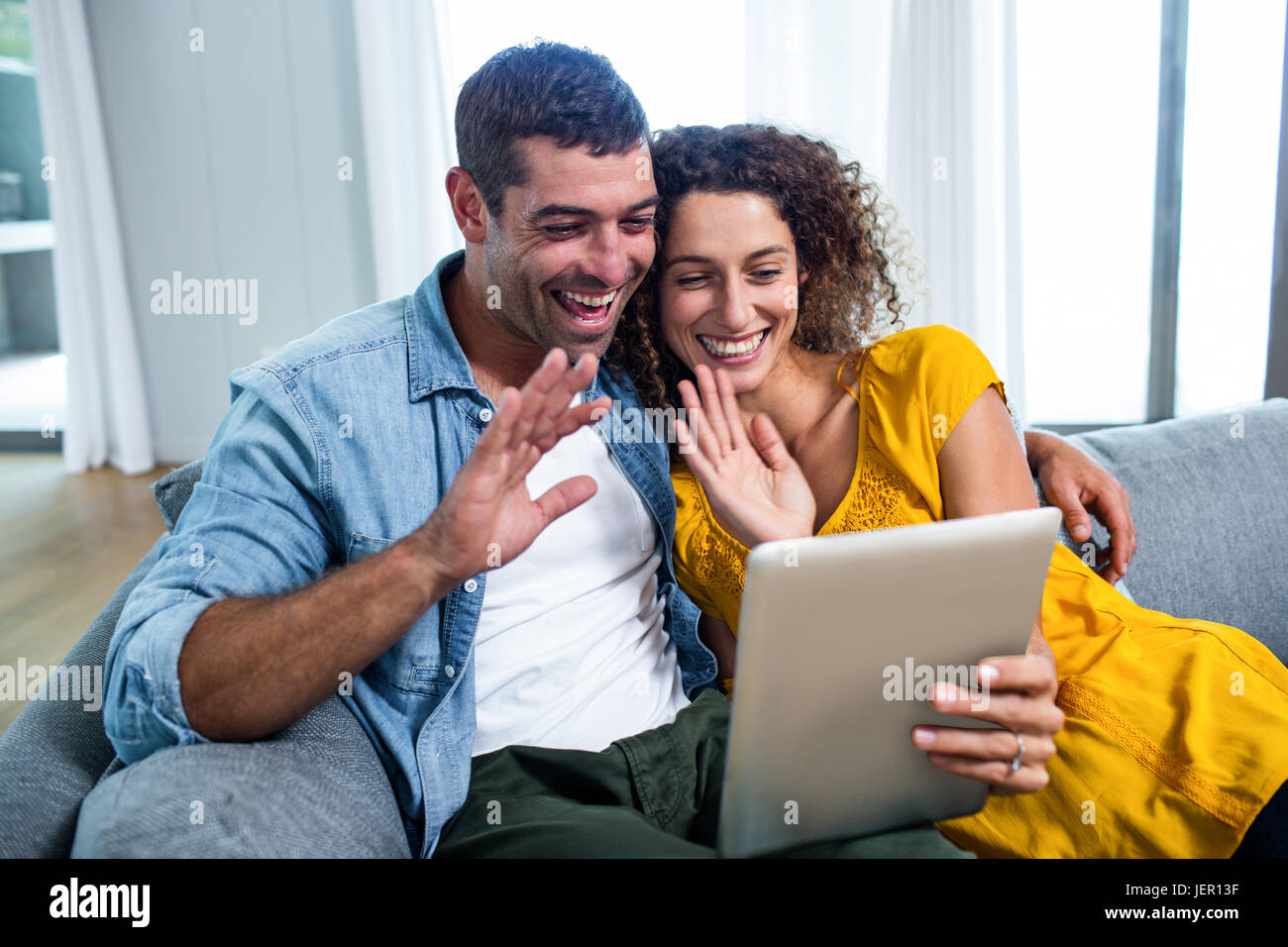 Happy couple using a digital tablet on sofa Stock Photo - Alamy