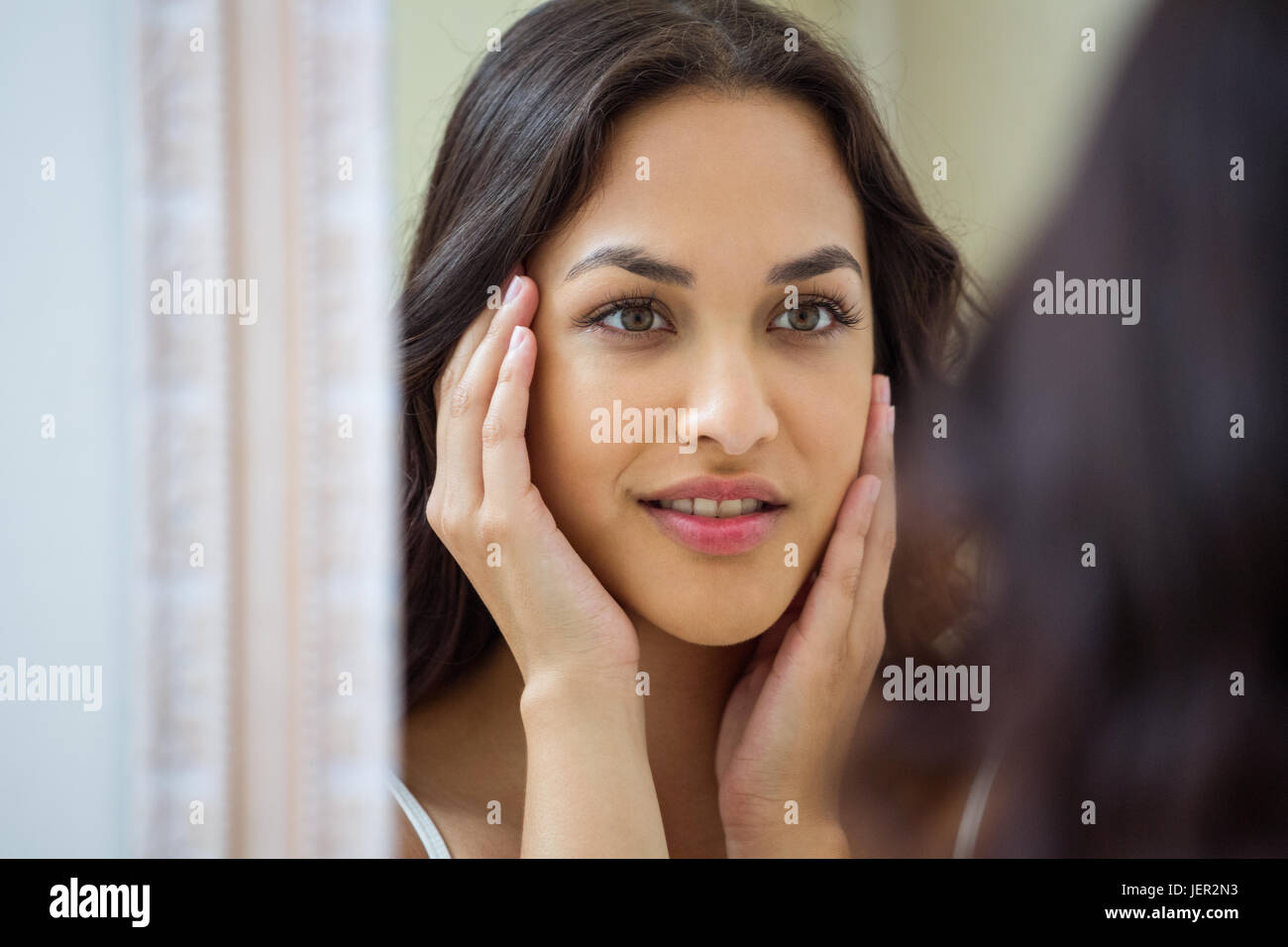 Young woman looking in mirror of bathroom Stock Photo - Alamy