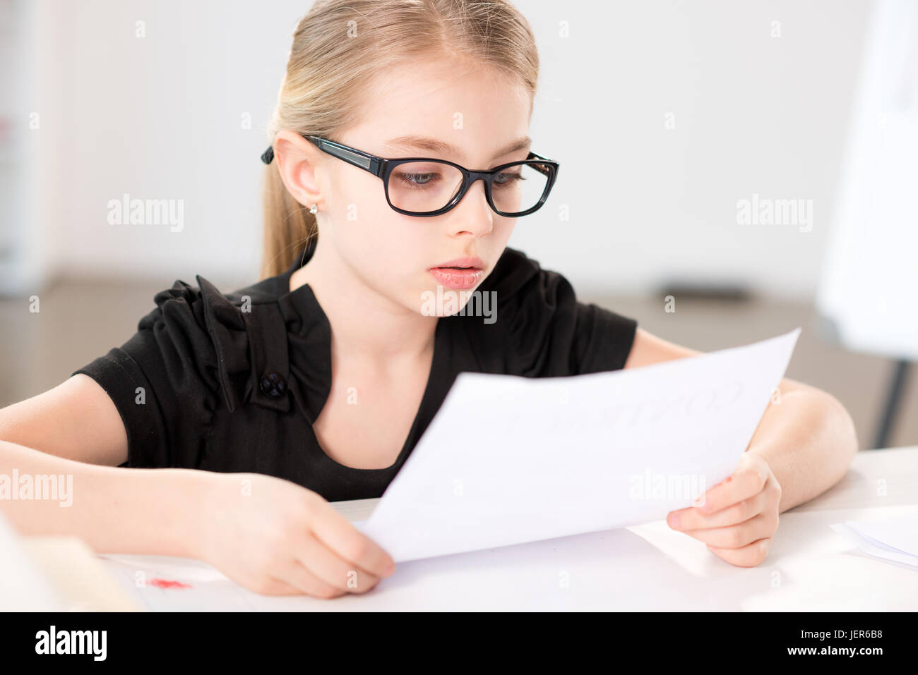 Little girl  sitting at table with papers in bright white room Stock Photo