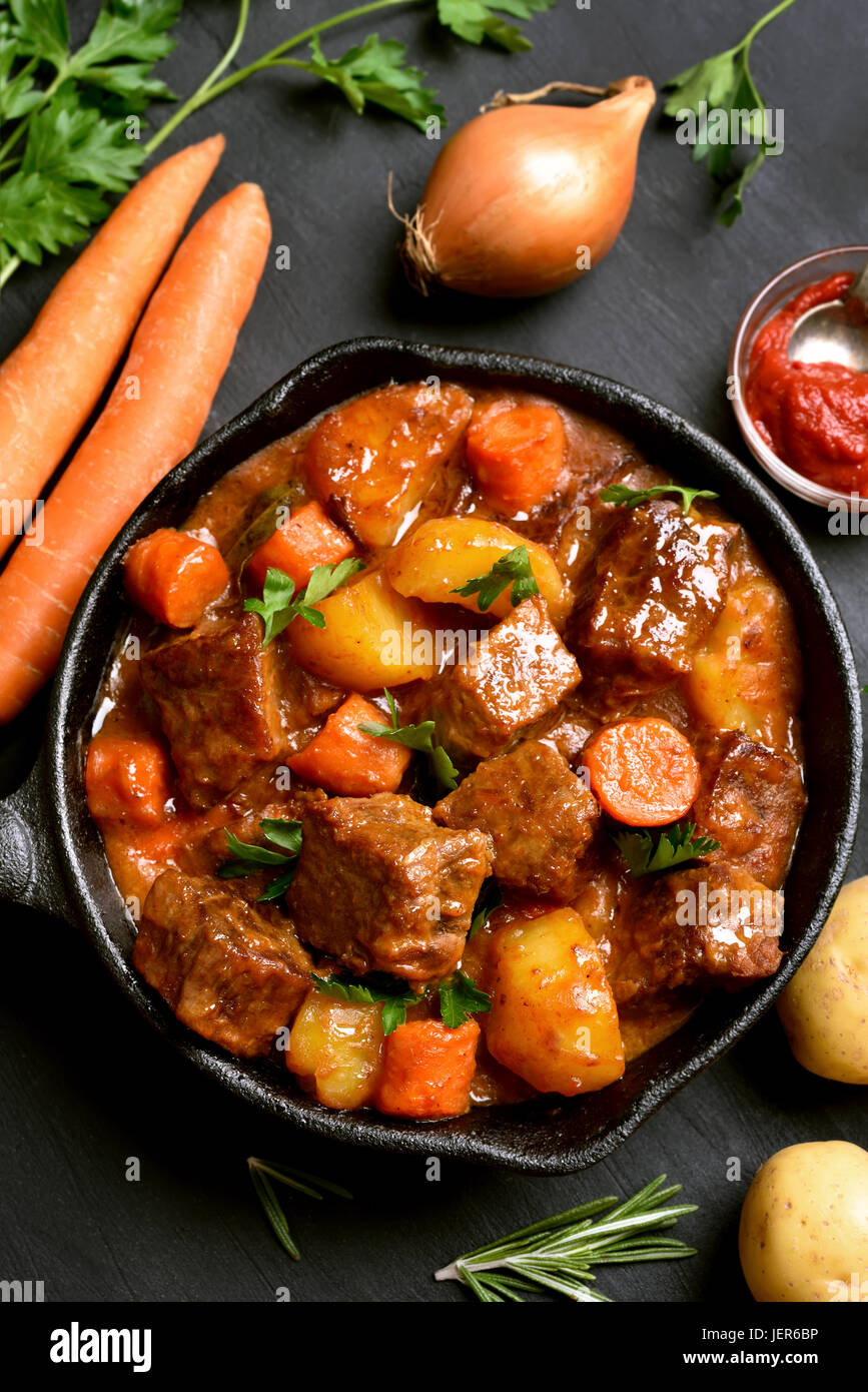Goulash, beef stew in cast iron pan on black background, top view Stock