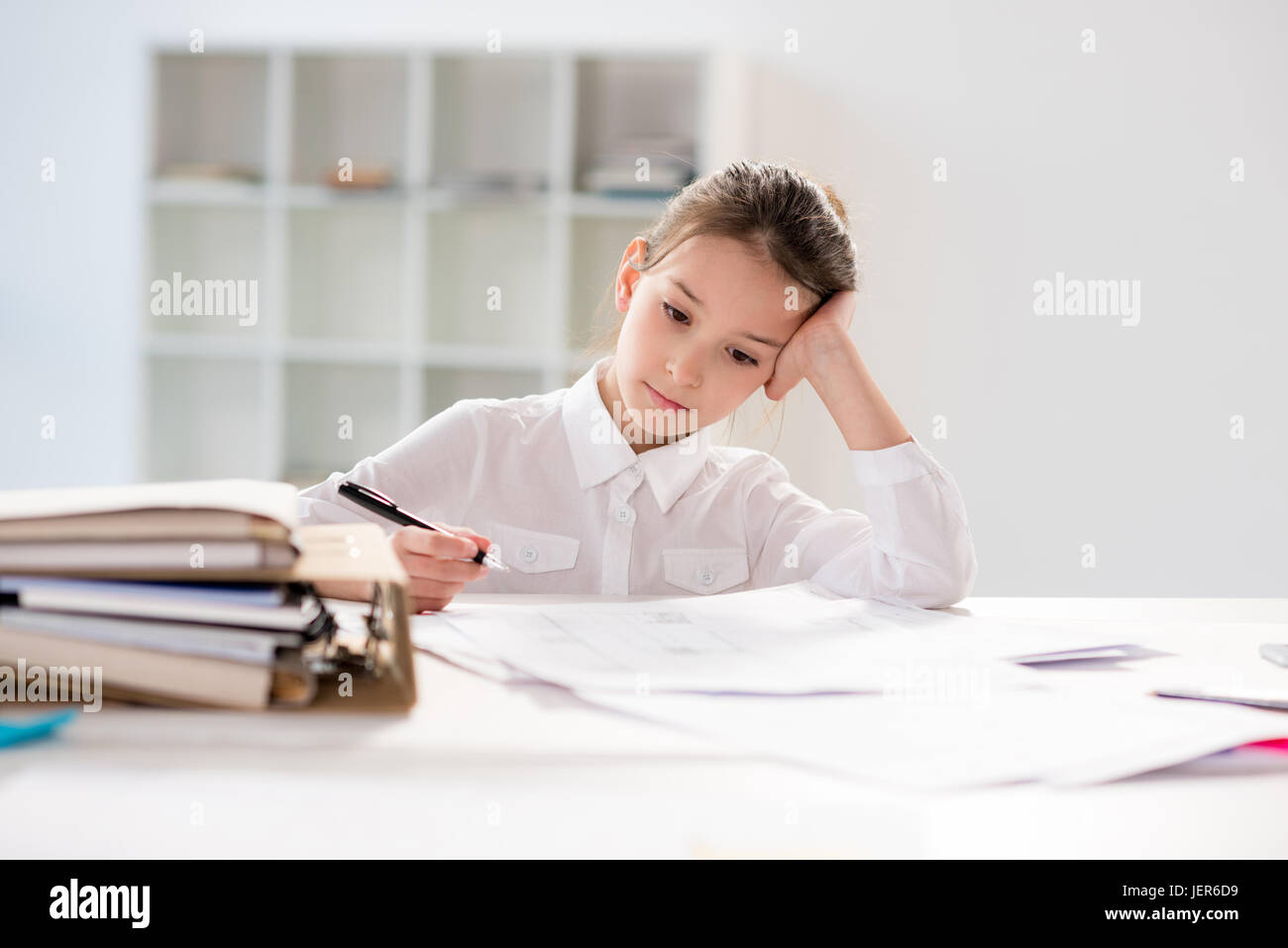 Little girl  sitting at table with papers in bright white room Stock Photo
