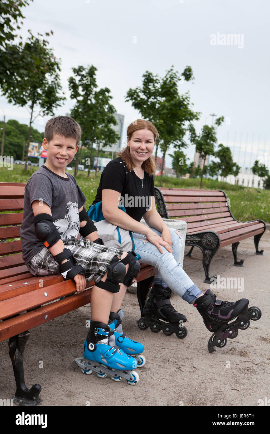 Mom and son are sitting, relaxing on a bench during rollerblading in the park Stock Photo