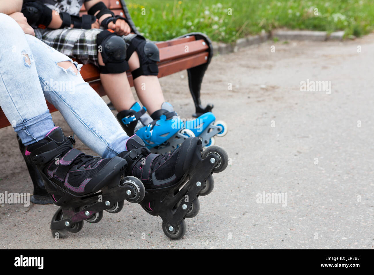 Close up view at the roller-skates wearing on female and boy legs, people sitting on the bench Stock Photo