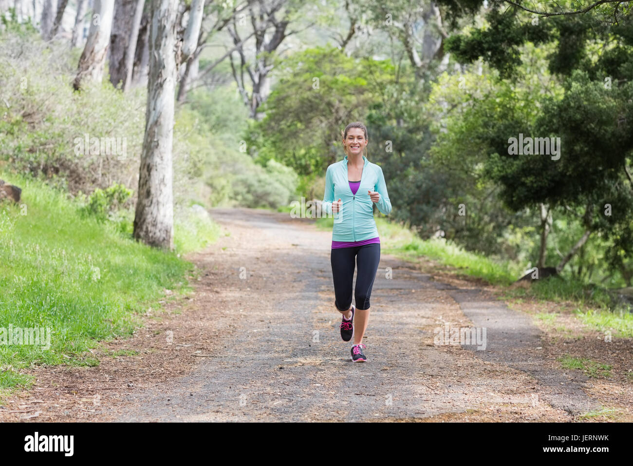 Cheerful young woman jogging in forest Stock Photo - Alamy