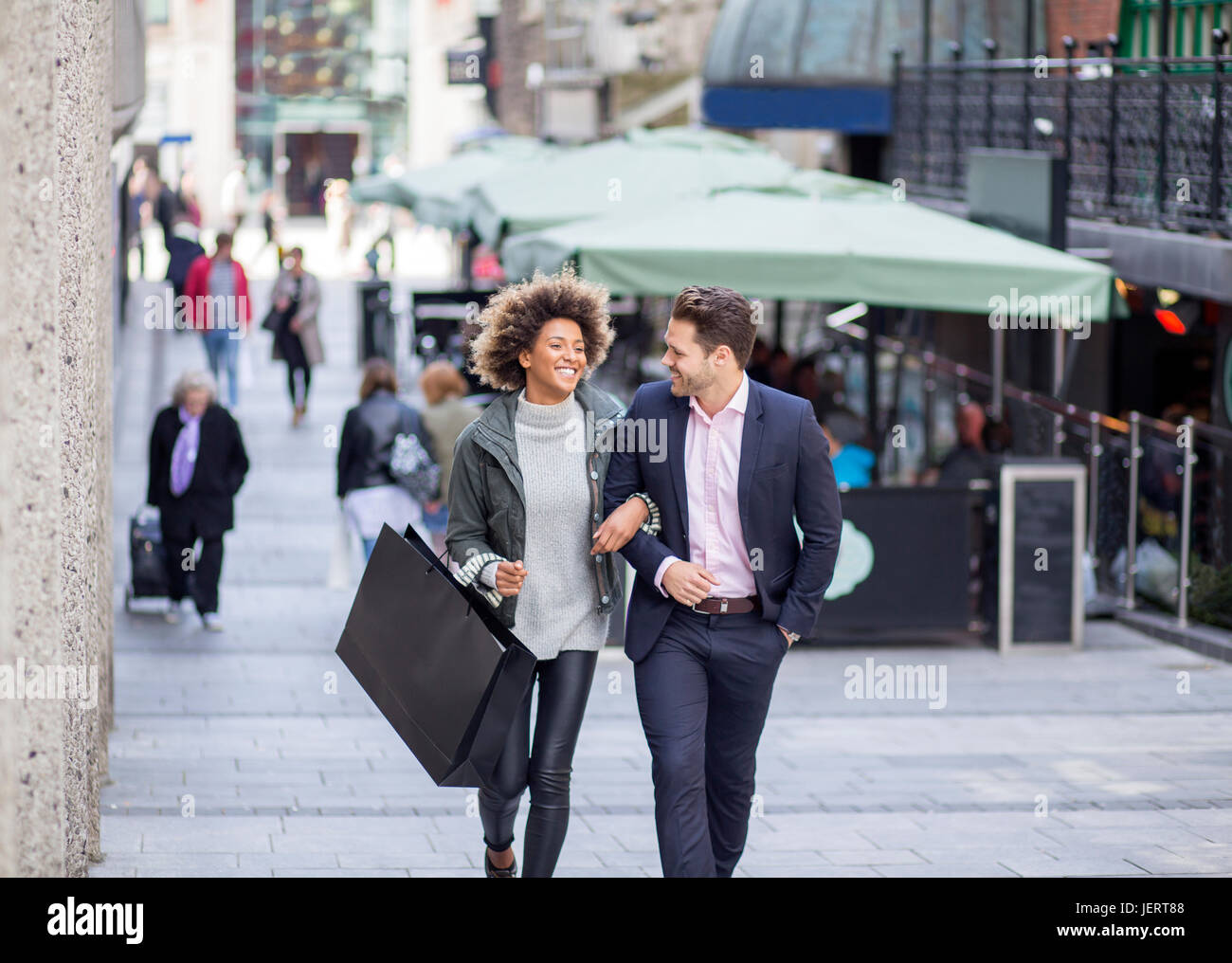 Couple in the city. They are walking arm in arm and the woman is holding a shopping bag. Stock Photo