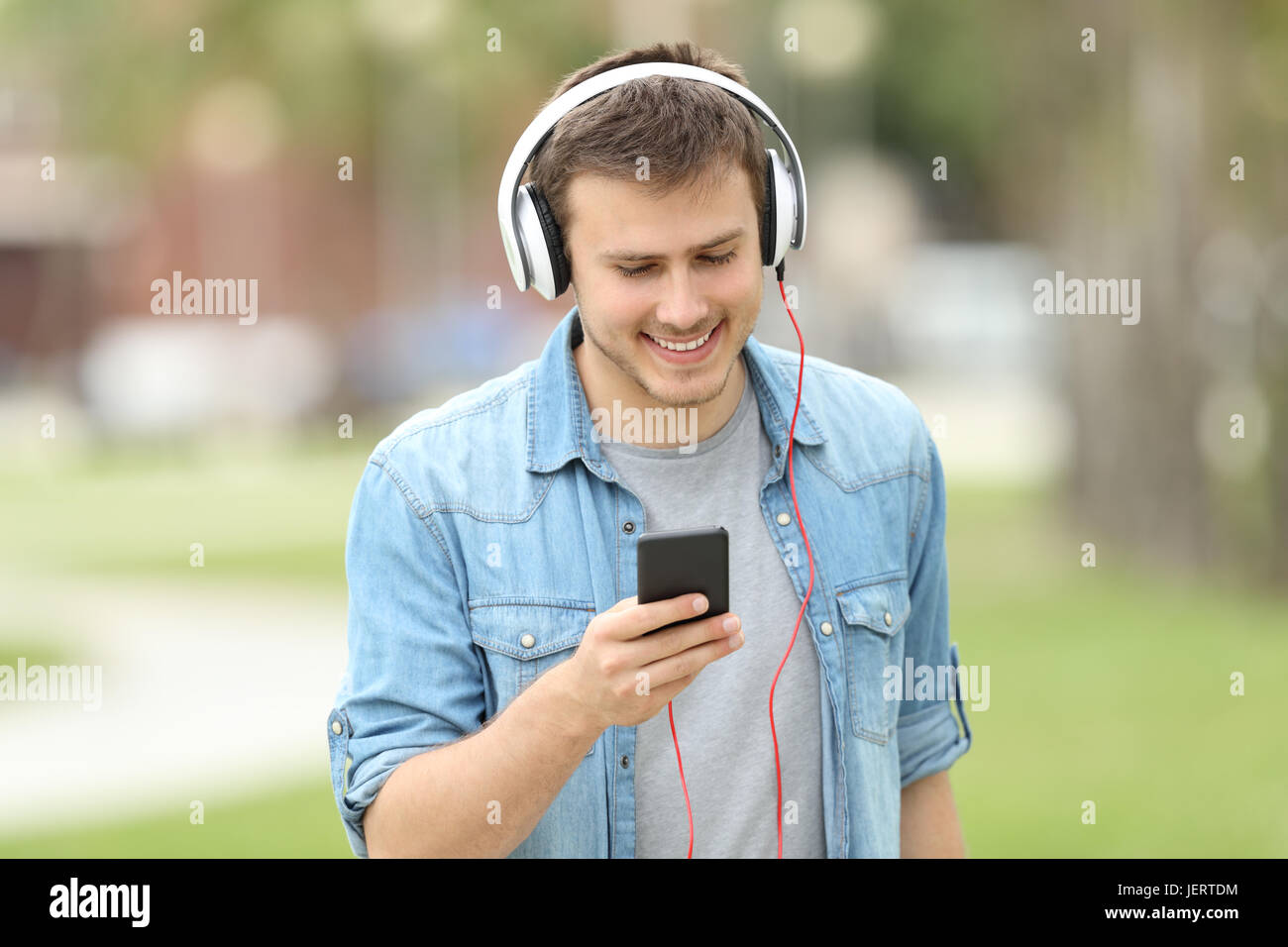 Front view of a teen boy walking towards camera and listening on line music outdoors in a park Stock Photo