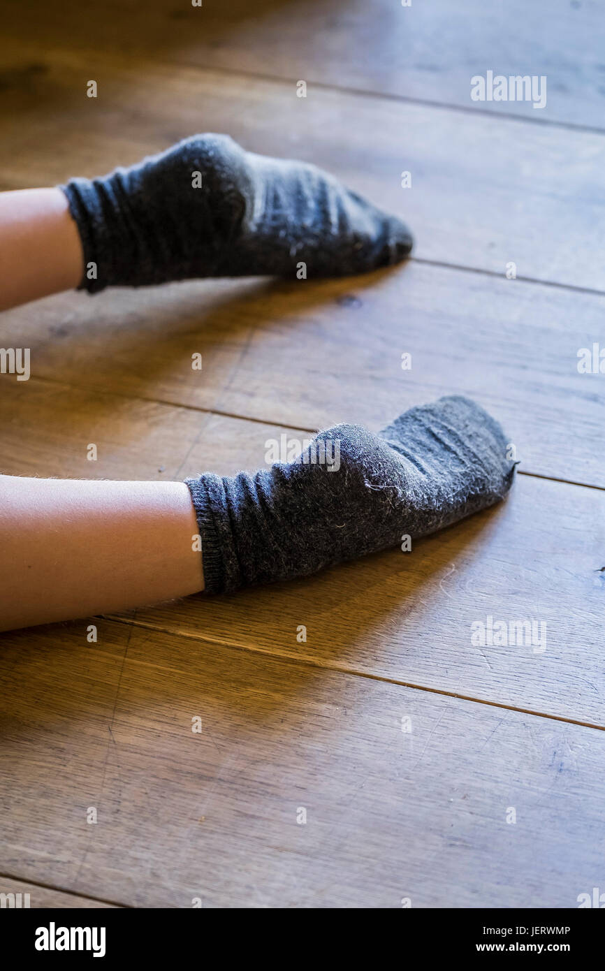 A young boy wearing socks and lying down on a wooden floor Stock