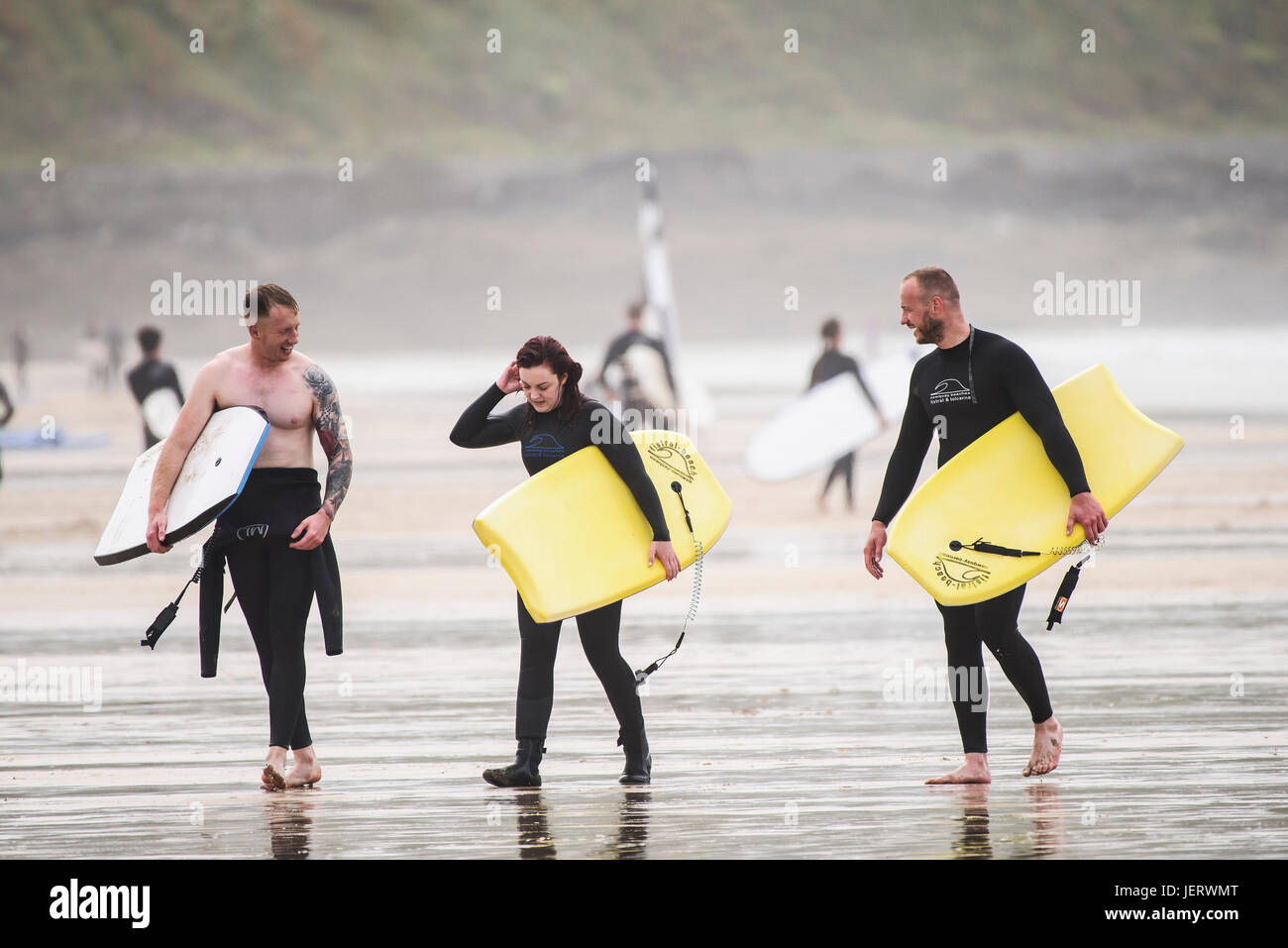 Three bodyboarders walking across Fistral Beach with their hired bodyboards. Stock Photo