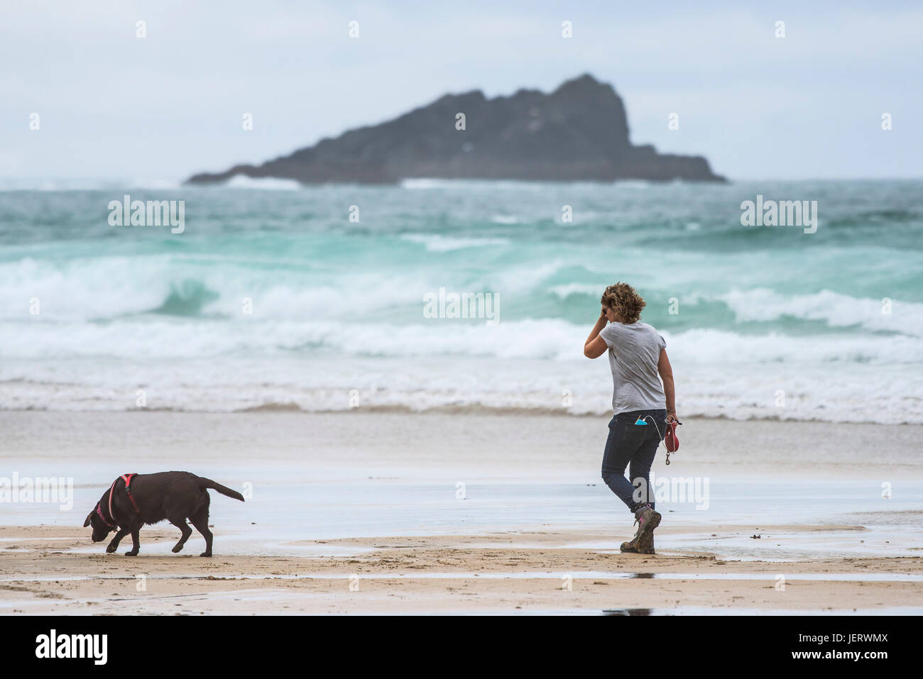 A woman walking her dog along dog friendly Fistral Beach in Newquay, Cornwall. Stock Photo