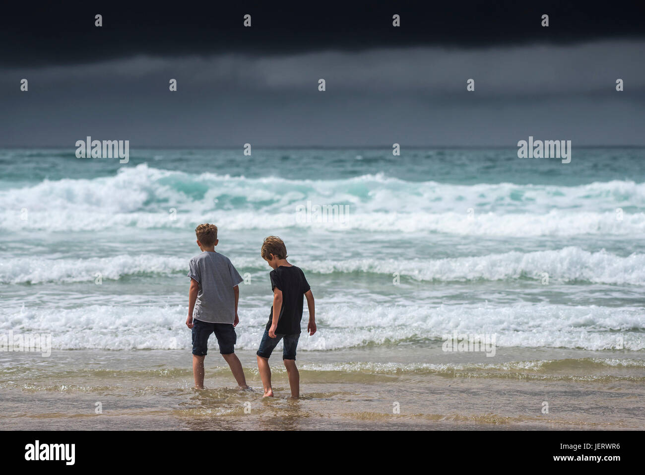 Dark rainclouds clouds gather as two young brothers paddle in the sea.  Weather UK. Stock Photo