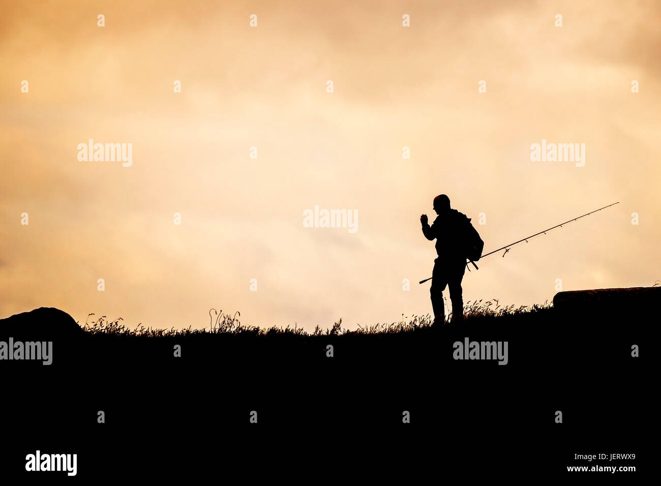 The silhouette of an angler looking for a spot to fish from on The Headland in Newquay, Cornwall. Stock Photo